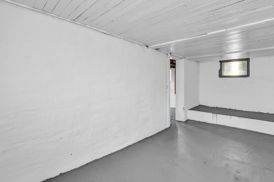 An empty basement room with painted walls, a grey concrete floor and a small window