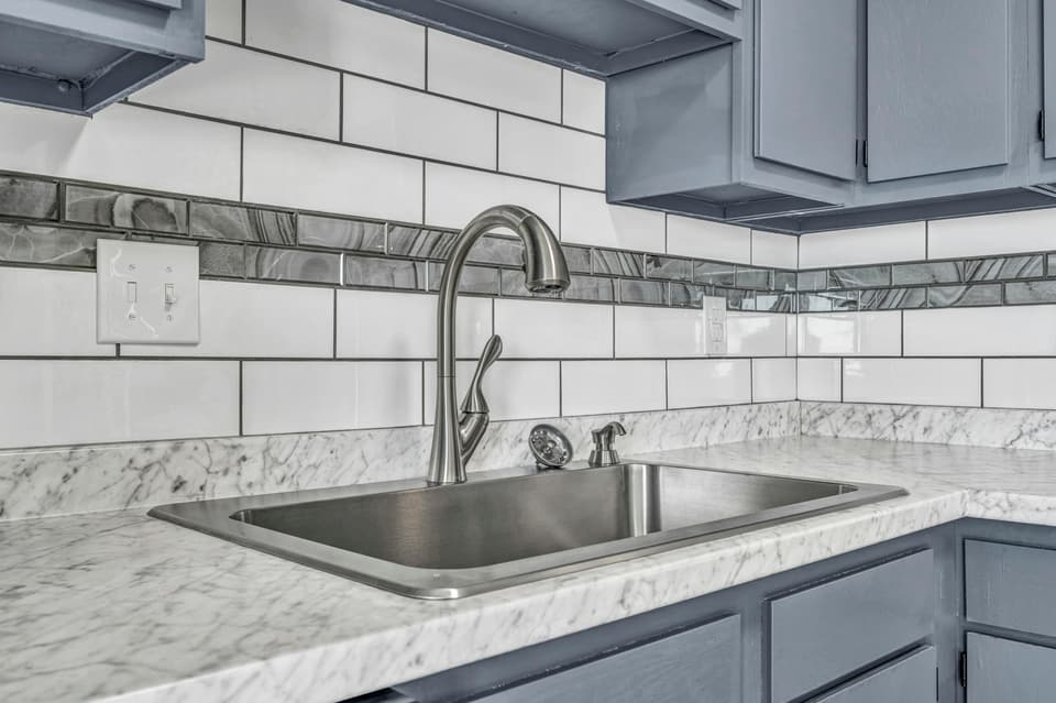 A stainless steel kitchen sink and faucet against white subway tile