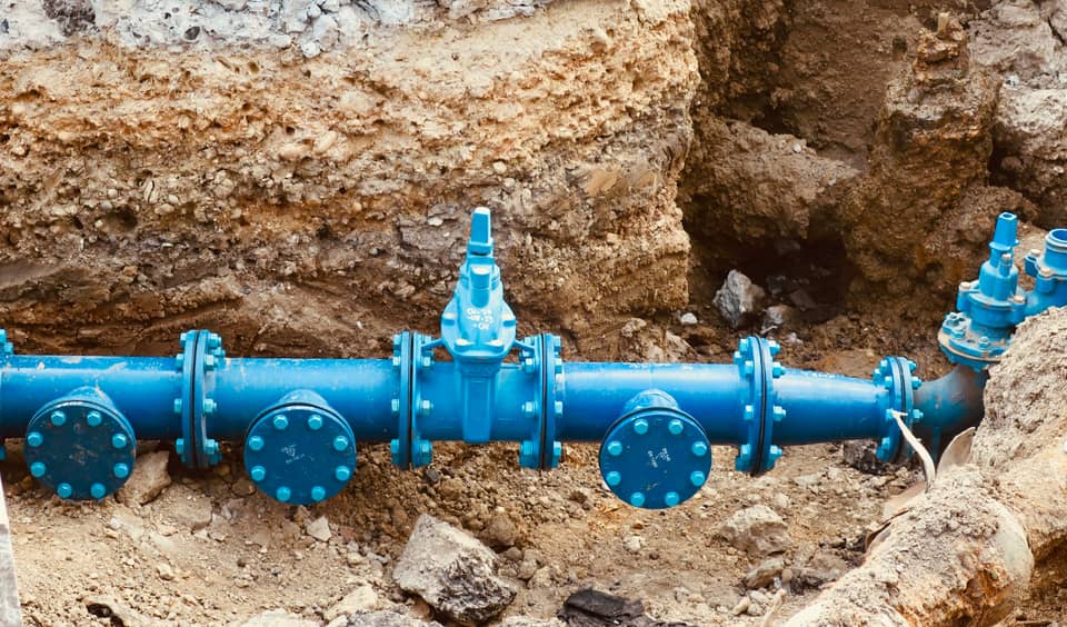 A blue water main with valves exposed in an excavated trench