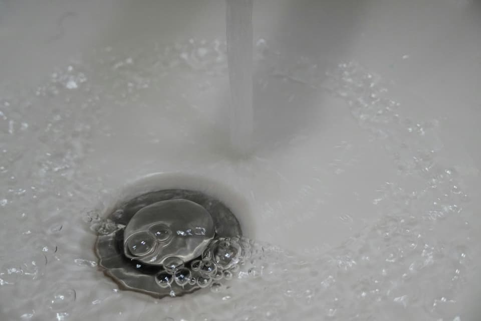 Water running from a tap into a white sink drain