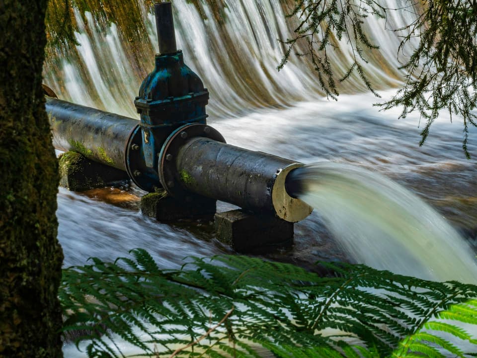 Water pouring from a large valved pipe below a weir